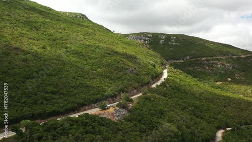 Aerial view of winding road through the lush green hills of Arrabida Natural Park in Portugal, showcasing the vibrant greenery and natural beauty of the landscape