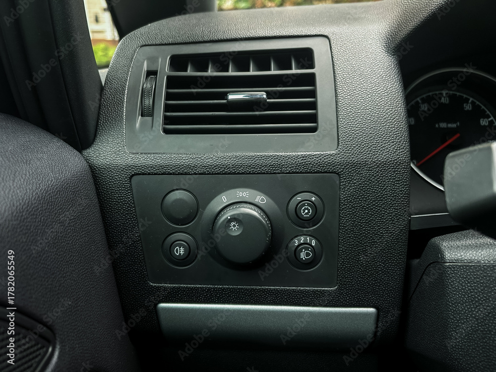 Fototapeta premium Close-up view of a car dashboard control panel showing various knobs and dials for adjusting air conditioning and lights, captured in a parked vehicle during daylight