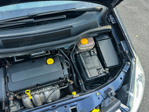 Car engine view showcasing essential components and maintenance details in a well-maintained vehicle located in a sunlit parking space