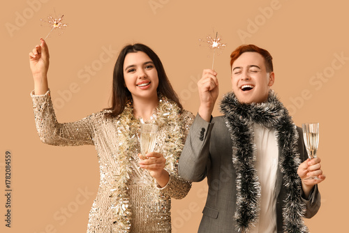 Young couple with Christmas tinsel, sparklers and glasses of champagne on bro...