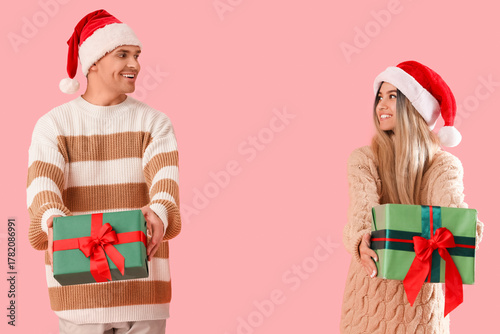 Happy young couple in Santa hats with Christmas presents on pink background