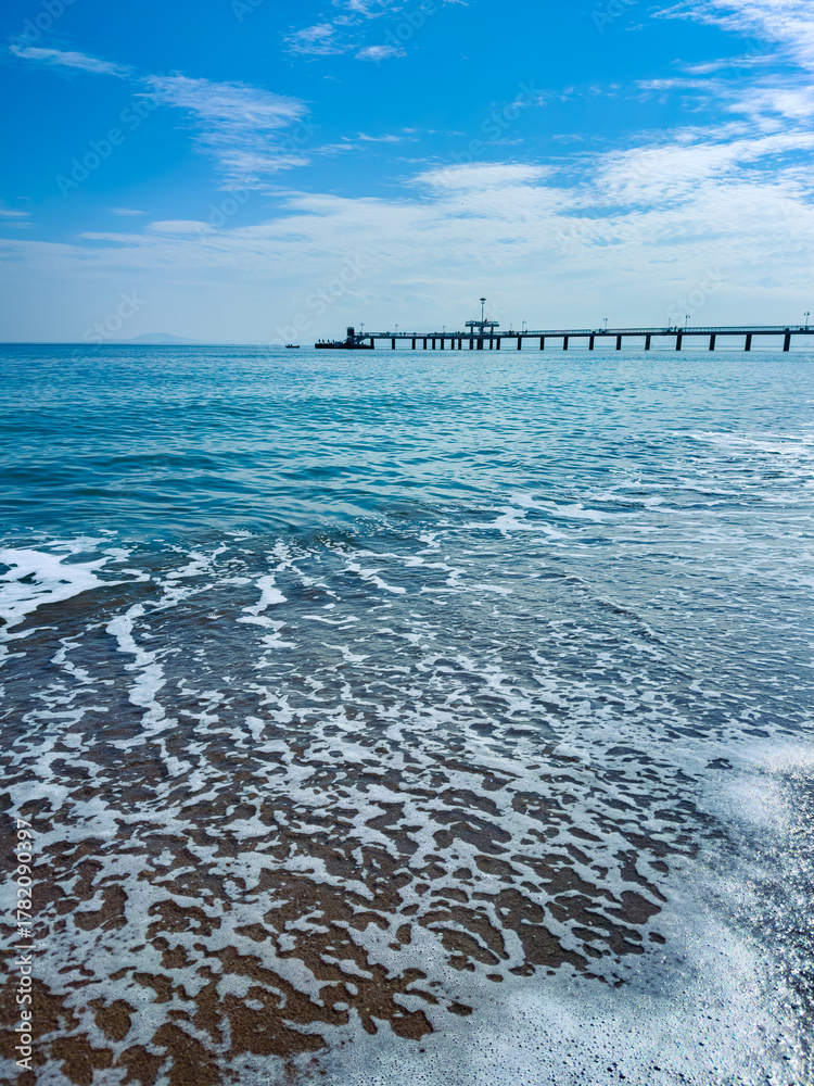 Fototapeta premium Endless waves meet serene sky at a coastal pier during a calm afternoon by the sea