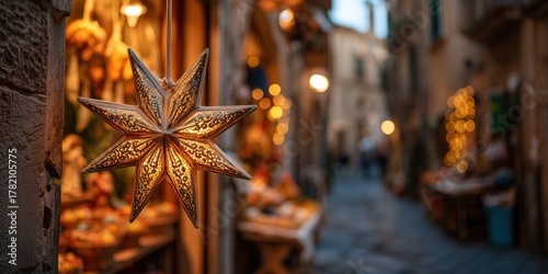 Fototapeta Naklejka Na Ścianę i Meble -  Bethlehem star decoration hangs on a lit street in a southern European town with stone buildings and holiday lights. Christmas atmosphere in a warm historic setting with festive decor.