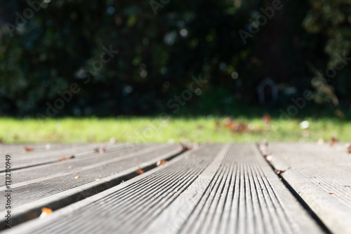 Plan rapproché d'un plancher en bois d'une terrasse avec jardin flou en arrière plan, format horizontal