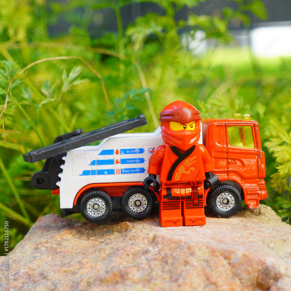 Fototapeta premium Lego Ninjago figure stands next to a toy tow truck on a rock