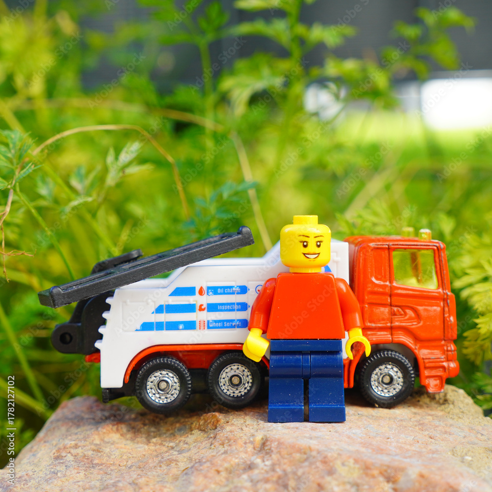 Obraz premium Lego figure stands proudly next to a toy tow truck on a rock