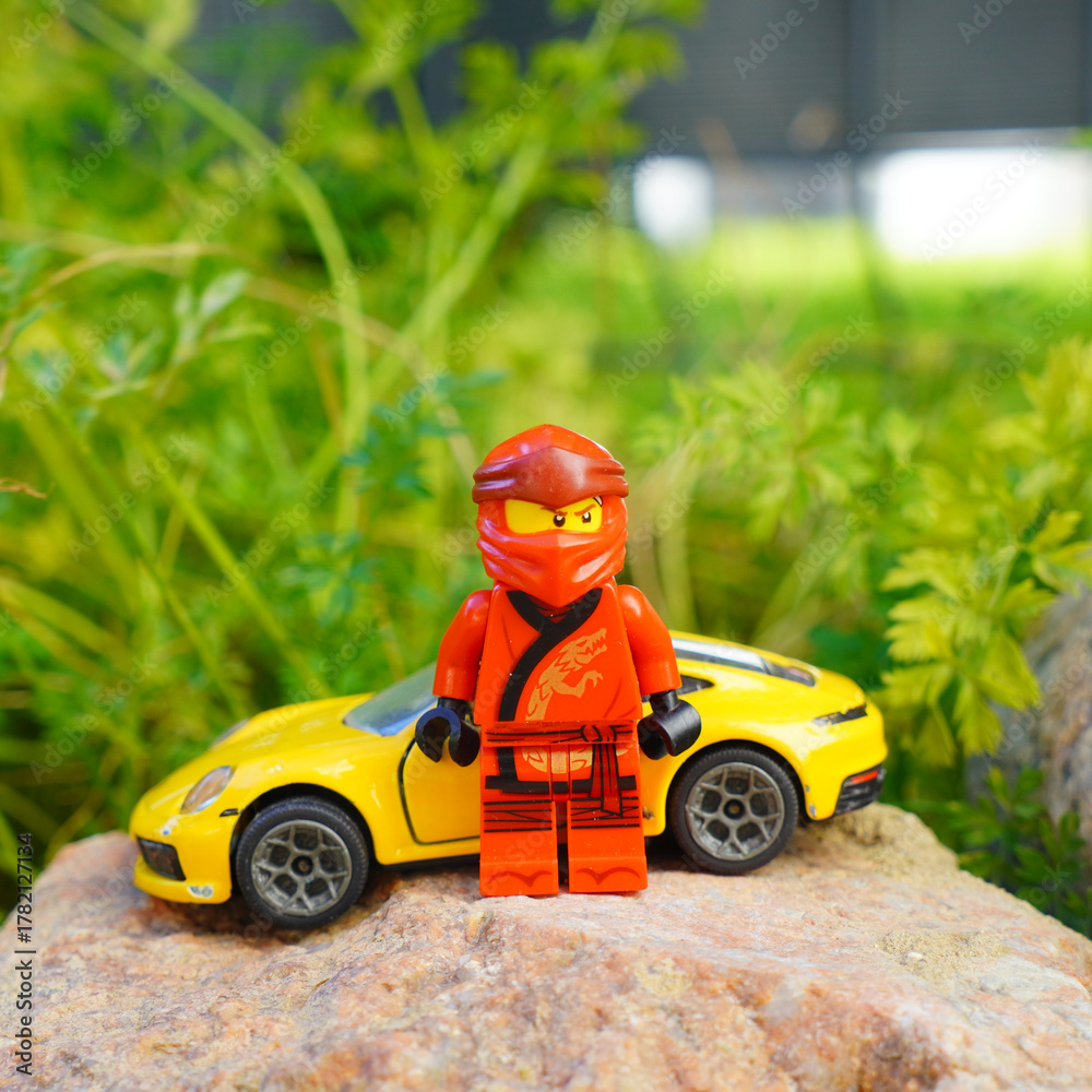 Obraz premium Lego Ninjago figure stands with a yellow sports car on a rock