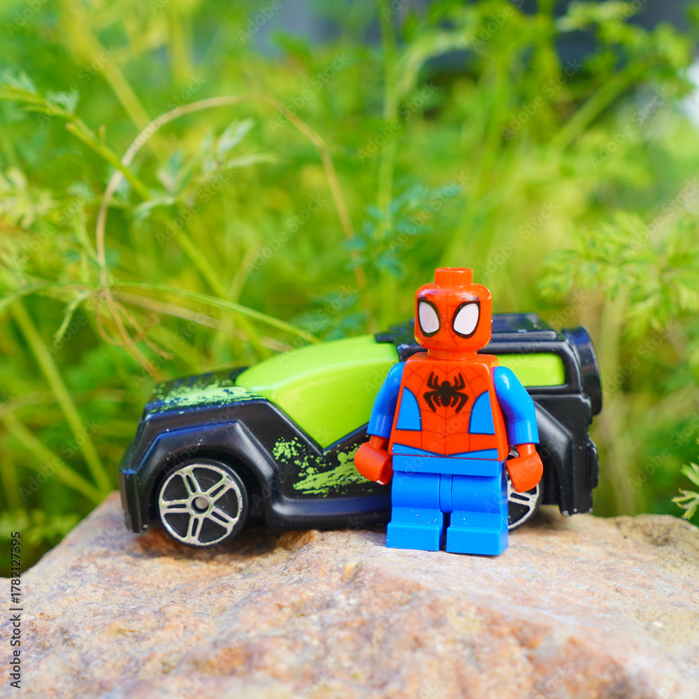 Obraz premium Spider-Man toy figure stands next to a toy car on a rock