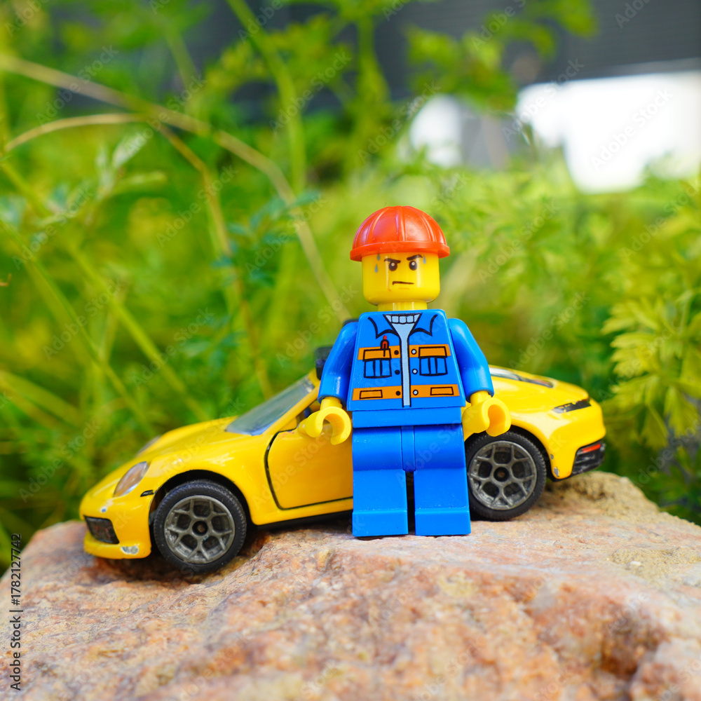 Obraz premium lego figure with yellow sports car on a rock with green foliage background