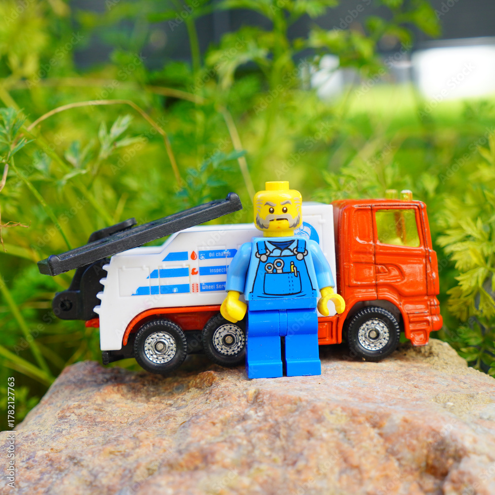 Obraz premium Lego mechanic figure stands next to a toy tow truck on a rock