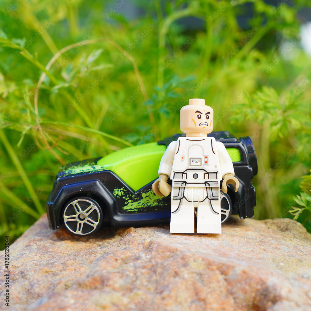 Naklejka premium Lego minifigure stands beside a toy car on a natural rock surface