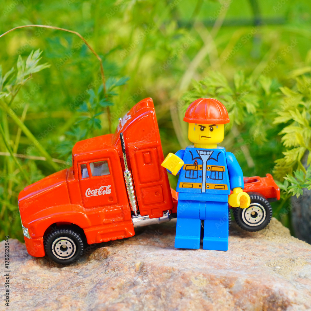 Naklejka premium Lego figure with a red Coca-Cola truck on a rock with green foliage