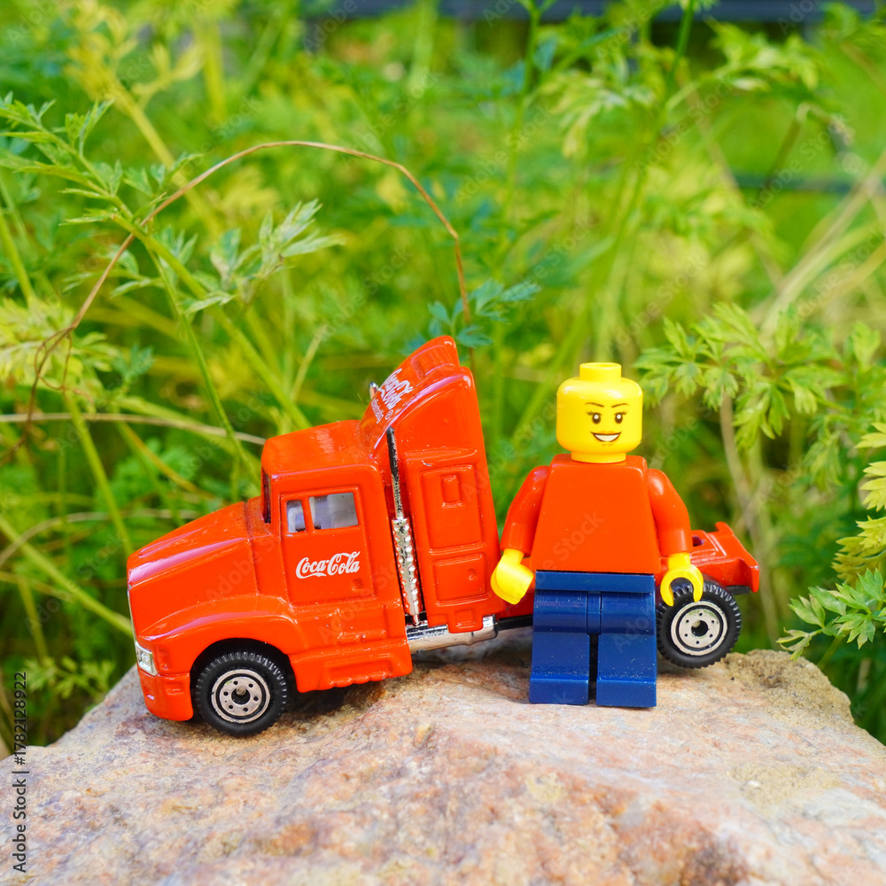 Naklejka premium Lego figure stands next to a Coca-Cola semi-truck toy on a rock