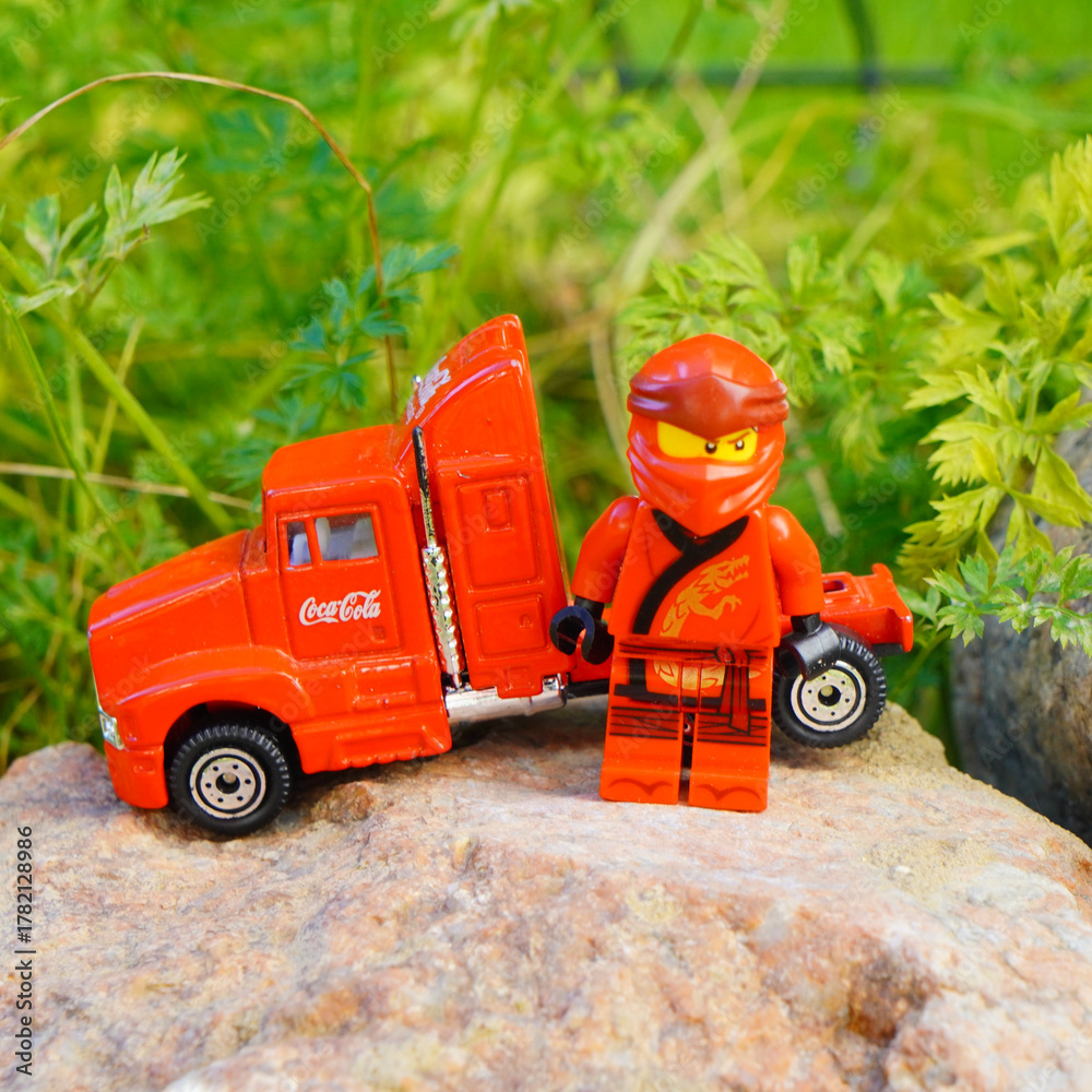 Naklejka premium Lego Ninjago figure stands next to a red Coca-Cola semi-truck toy on a rock