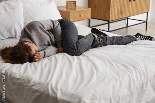 Sad young woman lying in be...