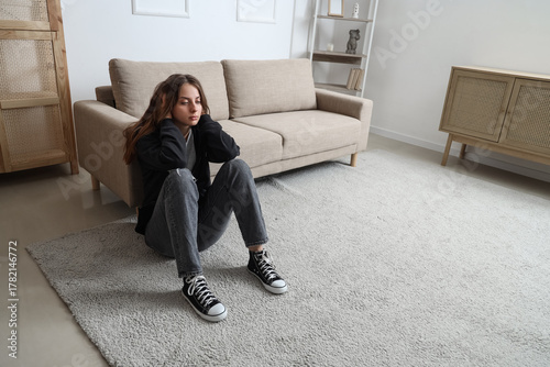Sad young woman sitting on carpet at home
