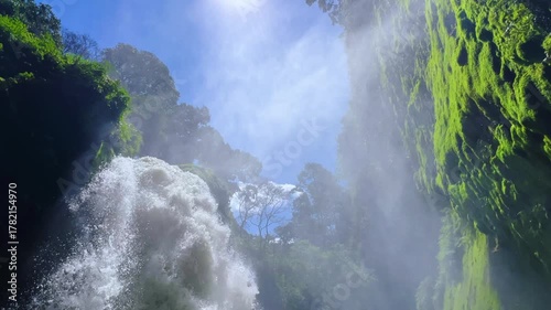 Blawan Waterfall around the Kawa Ijen Crater, hidden in the tropical jungle, East Java, Indonesia. A picturesque view of a powerful waterfall surrounded by sharp rocks covered with moss and plants. 4К