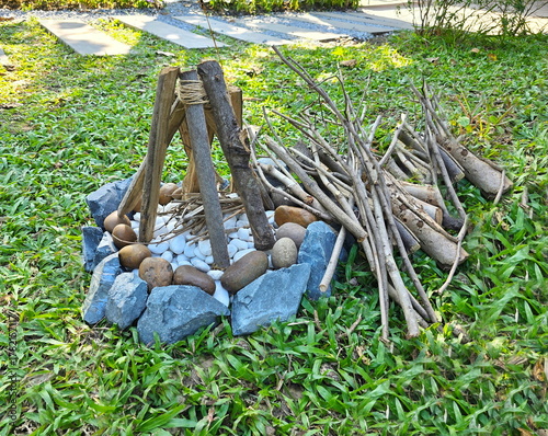 A small artificial bonfire is placed in the garden to decorate place. Large grey and brown rocks are arranged in circle around small white rocks. Small pine logs are used to arrange them like bonfire.