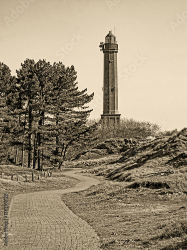 Sepia getönte Aufnahme eines Wanderwegs durch die Dünenlandschaft zum Leuchtturm auf der Insel Norderneys, Deutschland. 