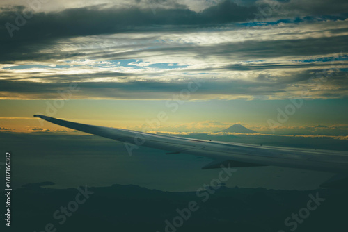 View of Mount Fuji from airplane window at sunset with wing and clouds