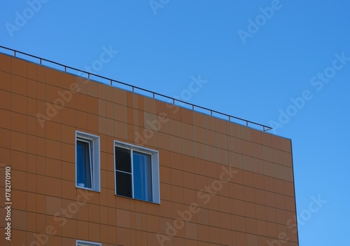 A modern building facade covered in orange square cladding panels against a clear blue sky.