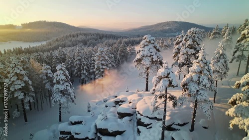 Snow-covered forested hill with rock formations at sunrise