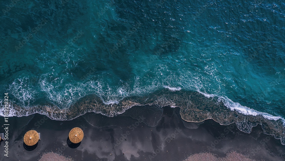 Fototapeta premium Aerial view of black sand beach with turquoise waters and straw umbrellas, ideal for vacation travel