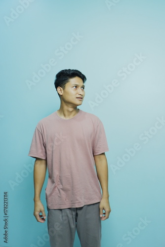 Pensive young man looking sideways against serene blue background, ideal for introspective campaigns or youth-focused marketing, modern style and simple