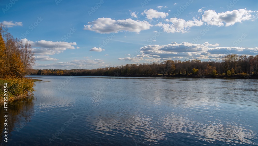 Fototapeta premium Uz River during autumn, reflecting trees and clouds in shallow water, highlighting urban density