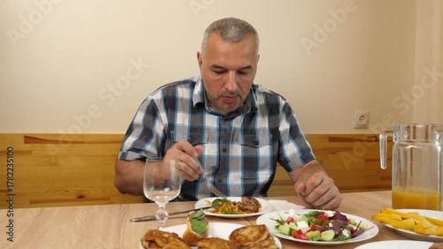 A man sits at the table in the kitchen, eating and drinking.