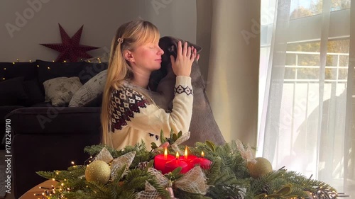 Woman in a Christmas sweater hugging a French bulldog by an Advent wreath with candles, cozy festive atmosphere, holiday with a pet