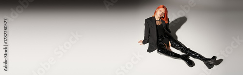 фотографія full length of sassy asian woman in sexy latex boots and blazer sitting on grey