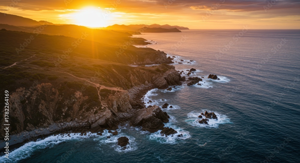 Naklejka premium Brilliant sunlight illuminates rugged coastline meeting the deep blue ocean water at dusk