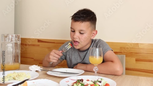 The boy is sitting at the table, eating delicious food and drinking juice.