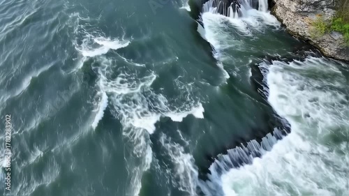 Aerial view of a powerful waterfall cascading into a river with foamy waves.