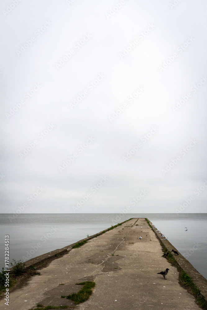 Fototapeta premium Old concrete pier under a cloudy sky in Nida, Curonian Spit and Curonian Lagoon, Lithuania