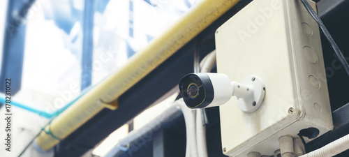 A modern white CCTV security camera mounted outdoors on a building with an electrical box, representing surveillance, protection, and modern technology.