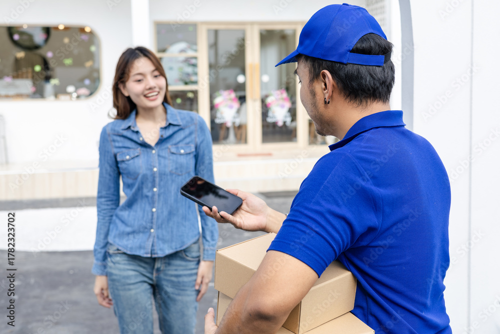 Obraz premium Delivery man handing parcel boxes to Asian customer woman at house gate, friendly courier representing reliable logistics, customer satisfaction, and small business delivery service partnership