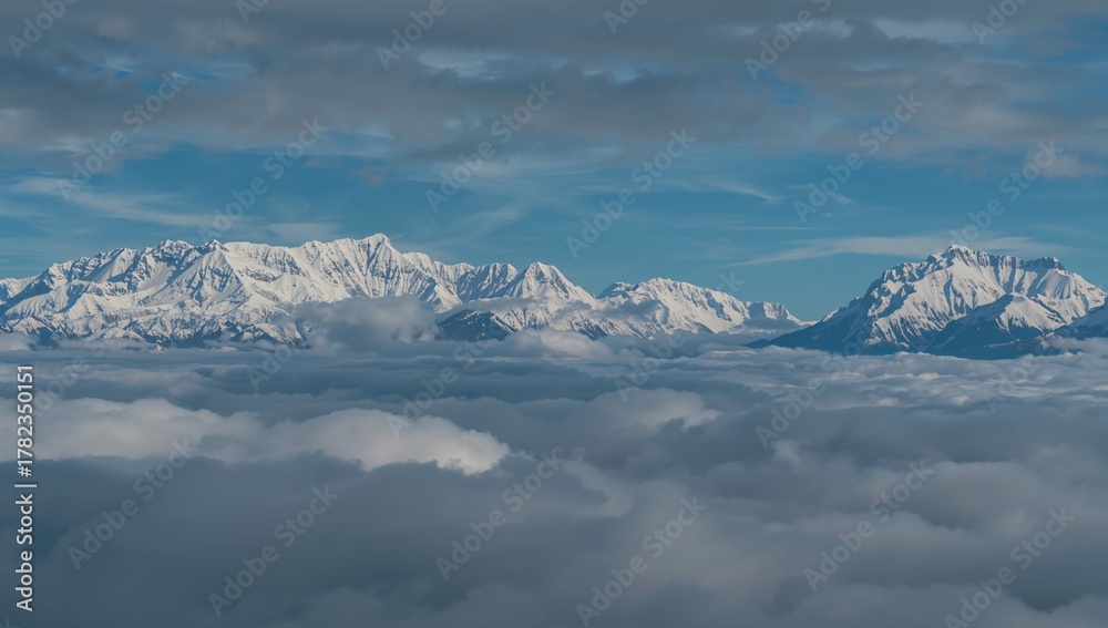 Obraz premium Aerial view of snow-covered peaks enveloped in clouds, showcasing the tranquil allure of mountainous terrain