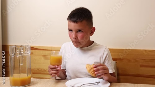 A boy eats and drinks juice while sitting at a table.