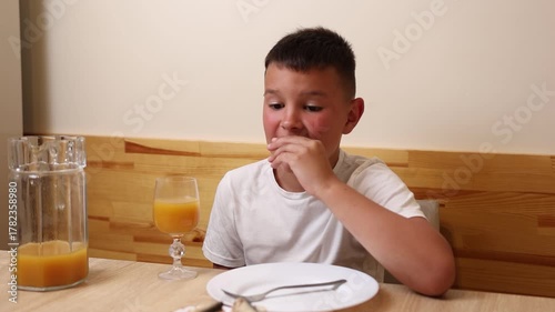 A boy eats and drinks juice while sitting at a table.