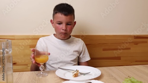 A boy eats and drinks juice while sitting at a table.
