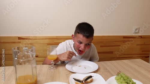 A boy eats and drinks juice while sitting at a table.