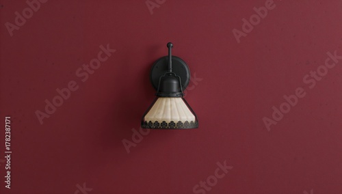 Fototapeta Naklejka Na Ścianę i Meble -  A small black light fixture with a white shade is attached to a red wall, decorative accent for vibrant interiors