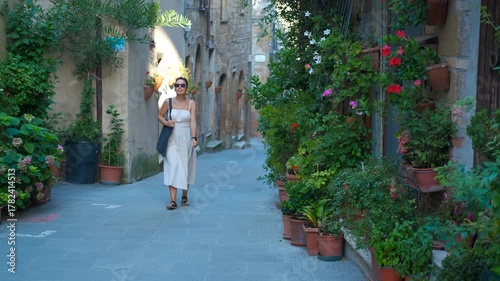 Elegant woman walking down charming italian alley. Beautiful woman in a summer dress walking through a narrow, picturesque alley in a historic italian town, admiring the charming architecture