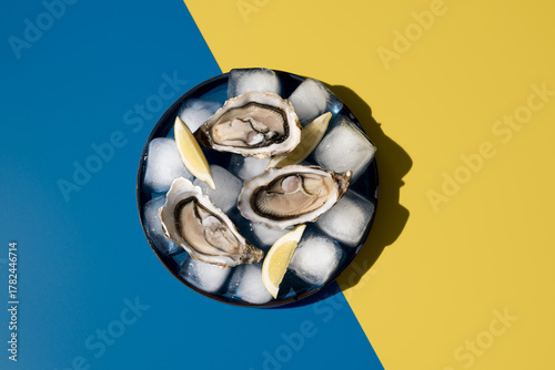 Photos Deliciosas ostras frescas con limón sobre hielo en un plato sobre un fondo azul y amarillo