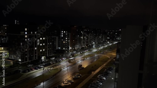 Street at night in quiet city neighborhood, illuminated residential buildings, wet asphalt with