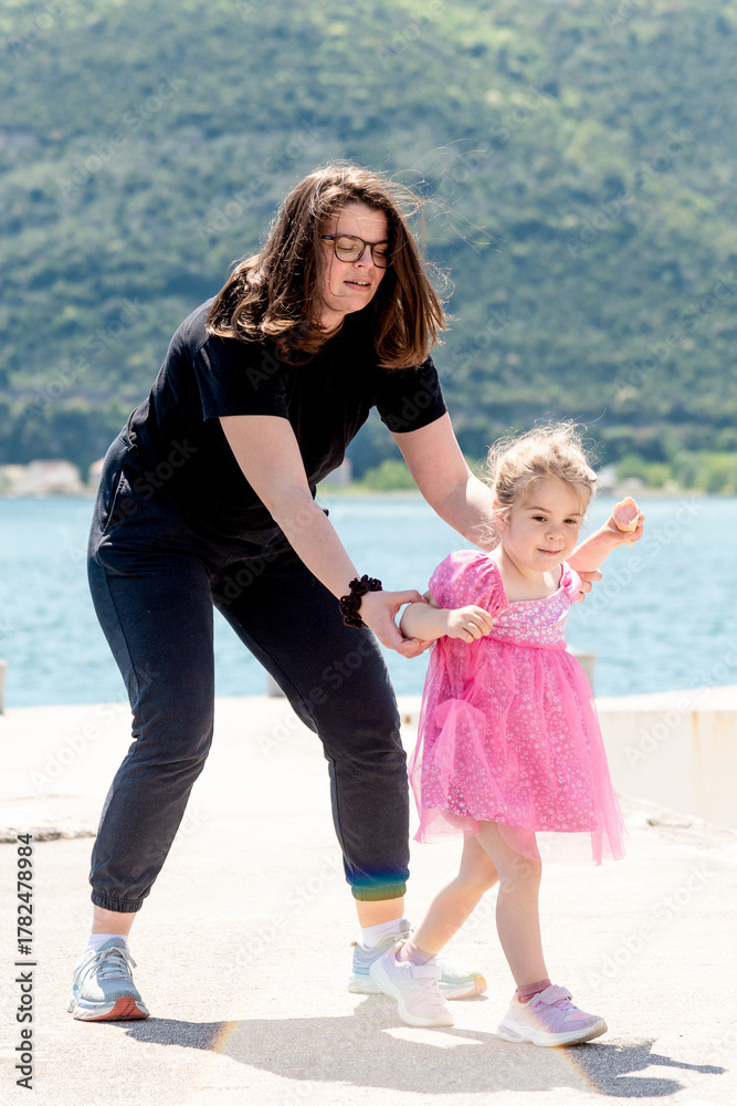 Fototapeta premium Mom and daughter family fooling around, woman and toddler girl walk in city park