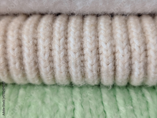 close-up stack of rolled cozy fabrics: white, beige ribbed knit and pale green knit