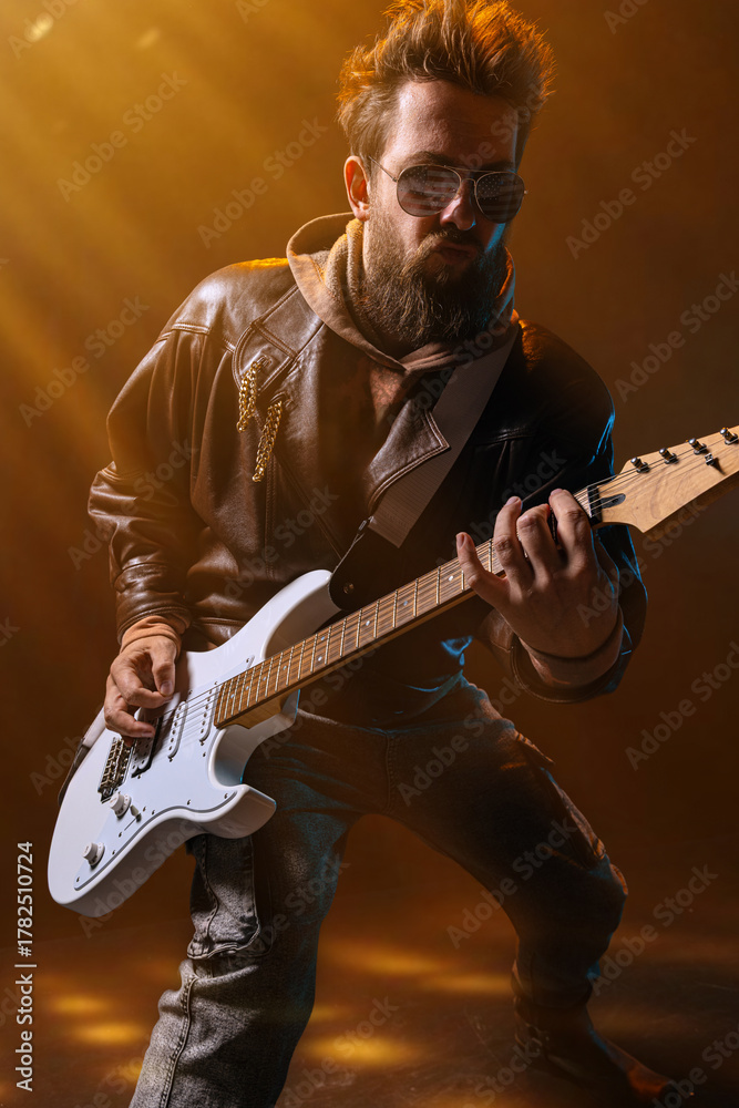 Obraz premium Male guitarist performing with intensity and focus in orange light beams. Concept of creative advertising, motivational campaigns, emotional health, and music education visuals.